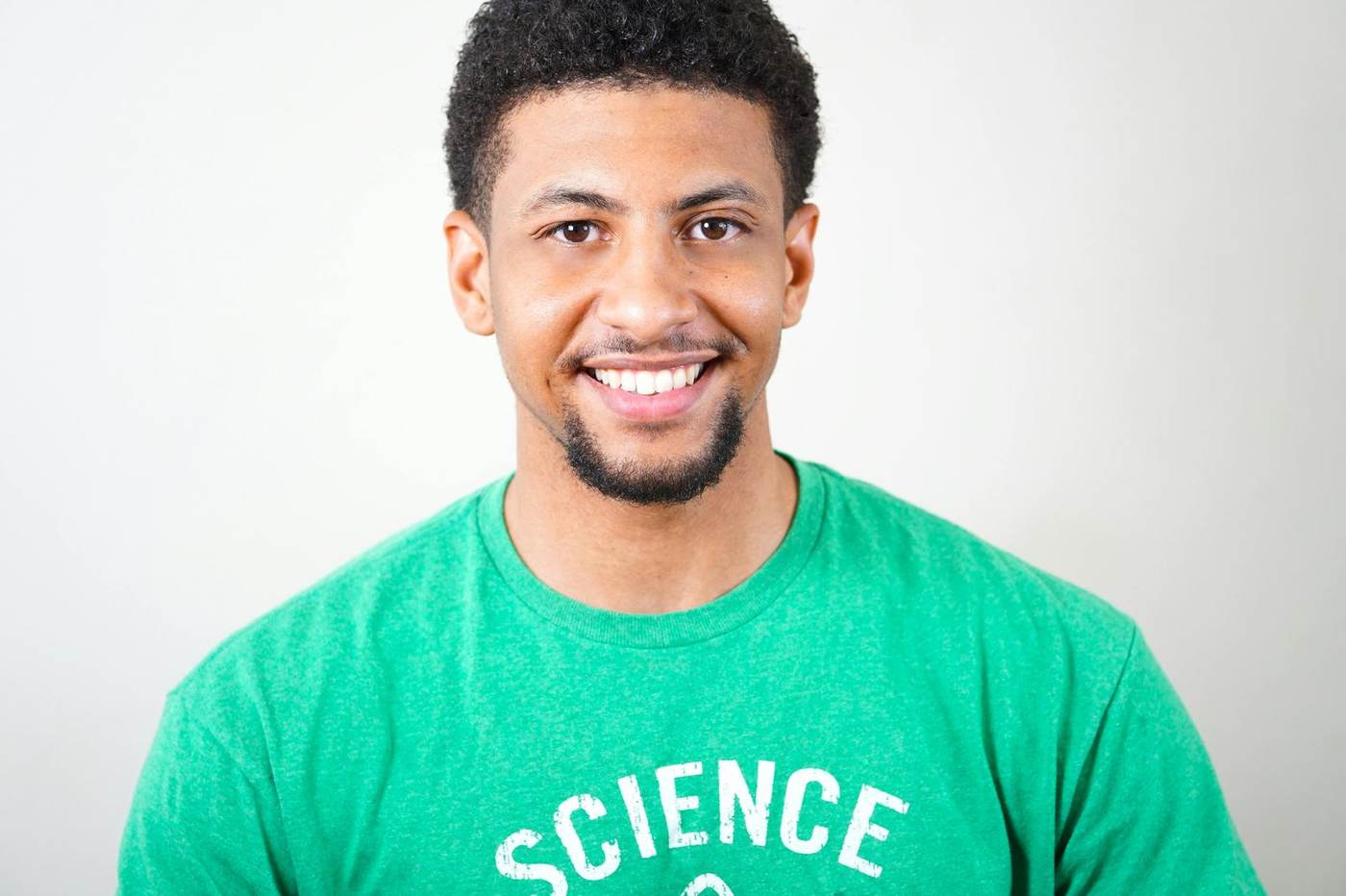 Smiling man with short dark curly hair and a goatee, wearing a green t-shirt that says "Science".